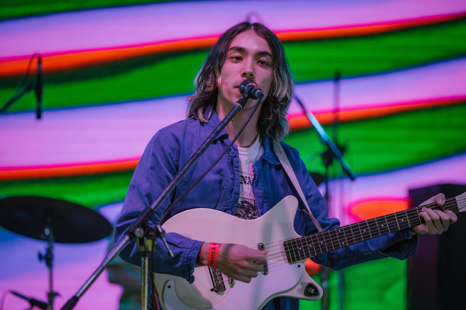 Guitarist singing in front of neon bands of colour