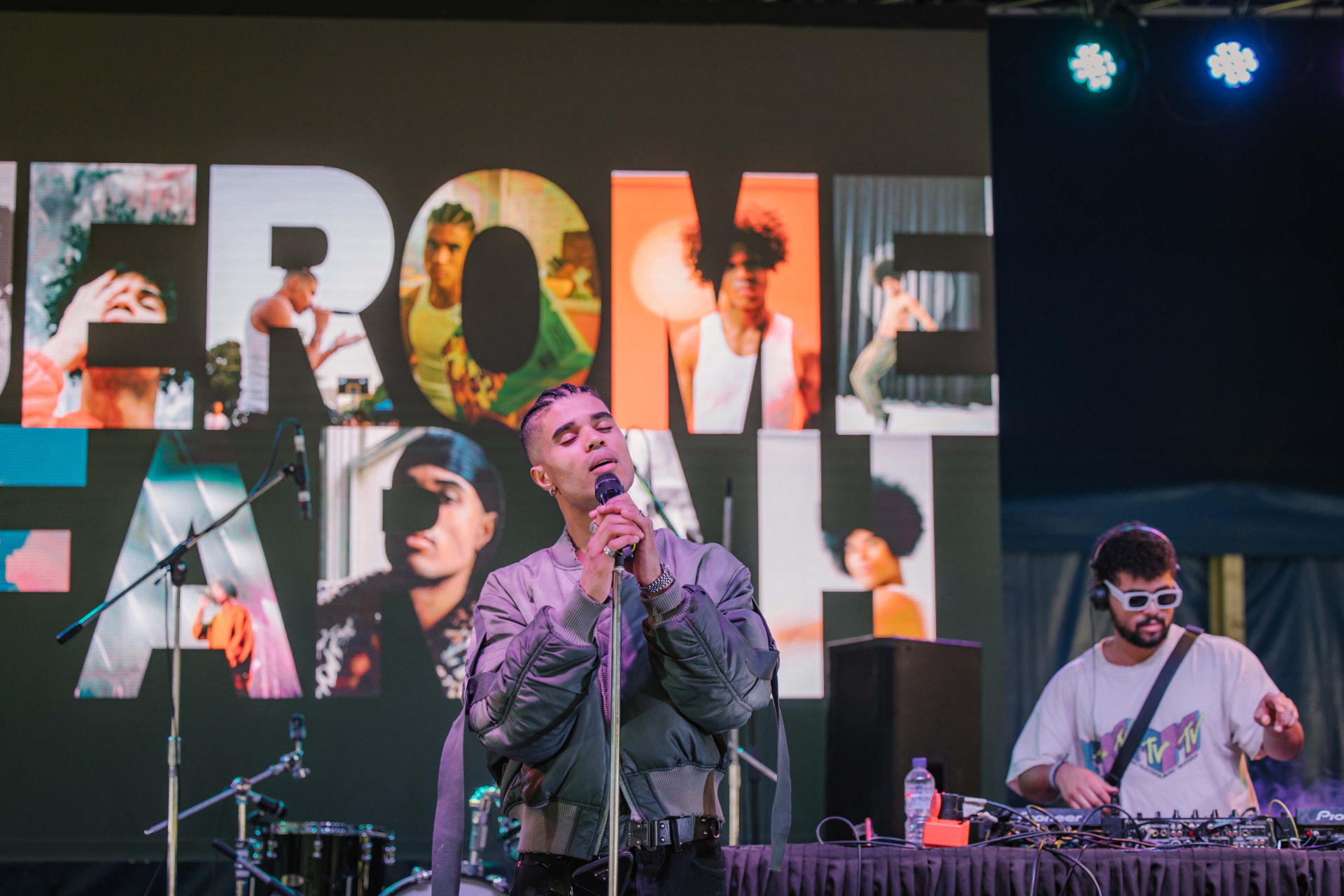 Vocalist singing beside a DJ at a festival stage