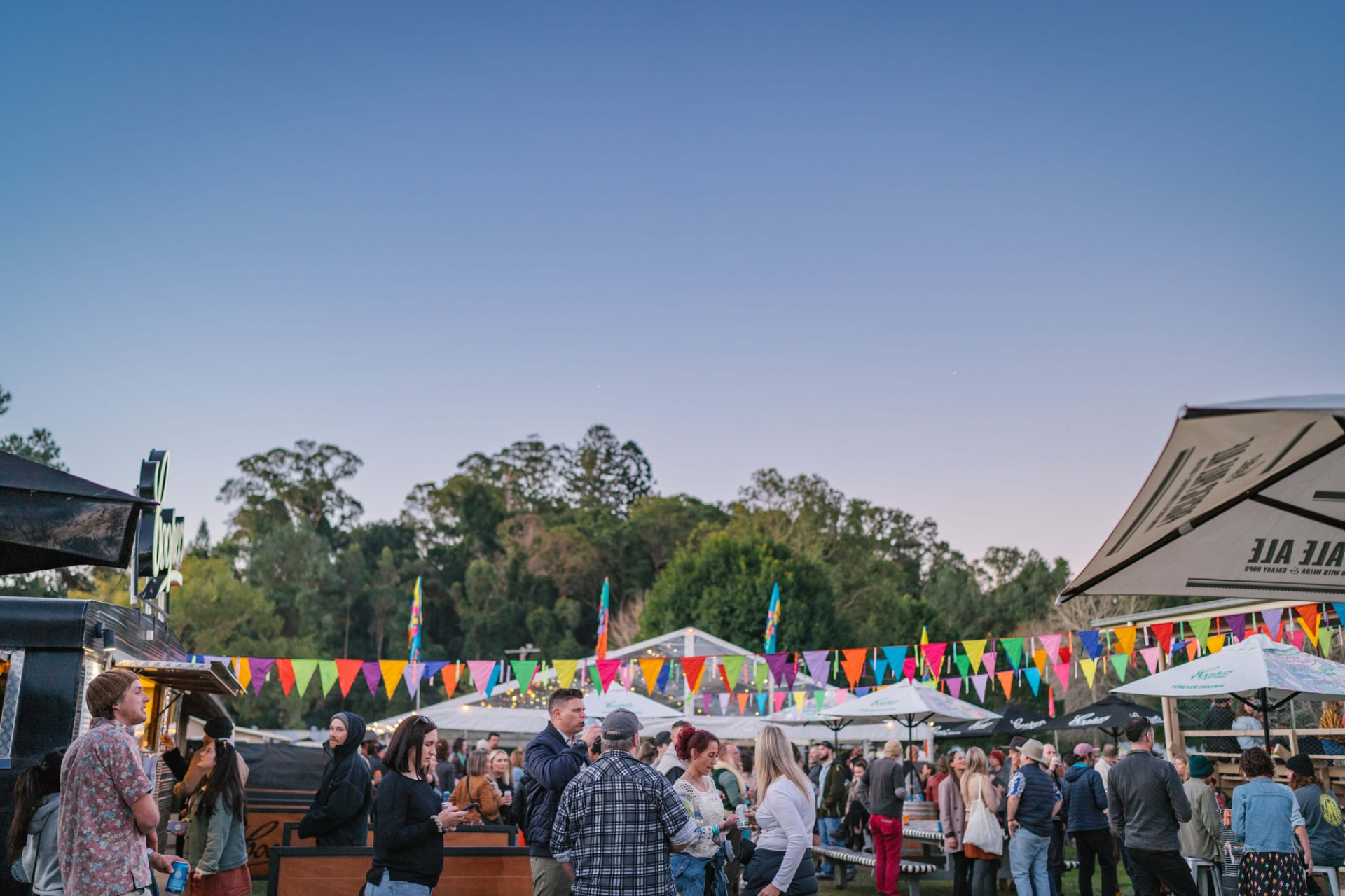 Festival-goers gathered among drink stalls and colourful bunting at dusk