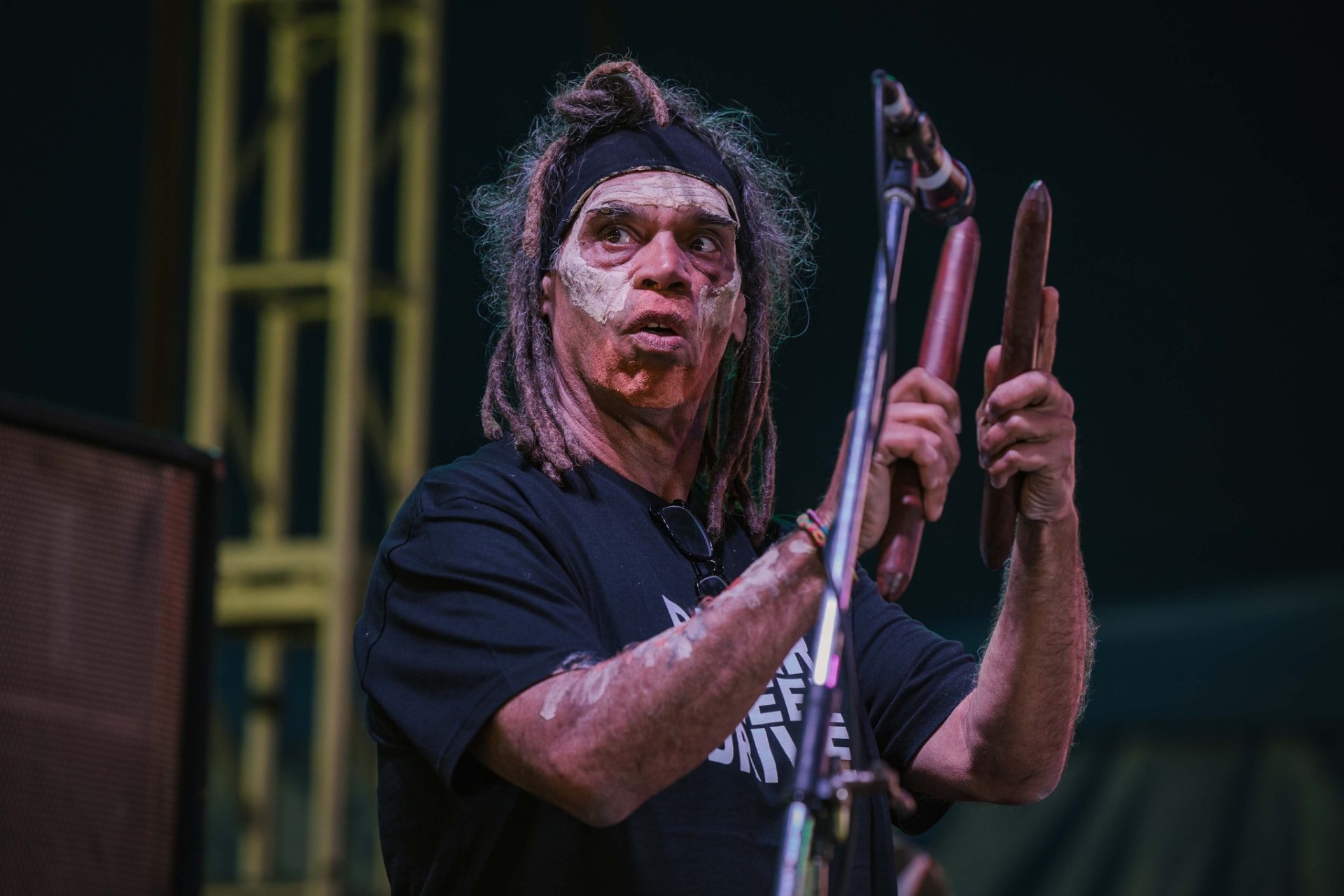 A First Nations musician playing clapsticks at the microphone on stage