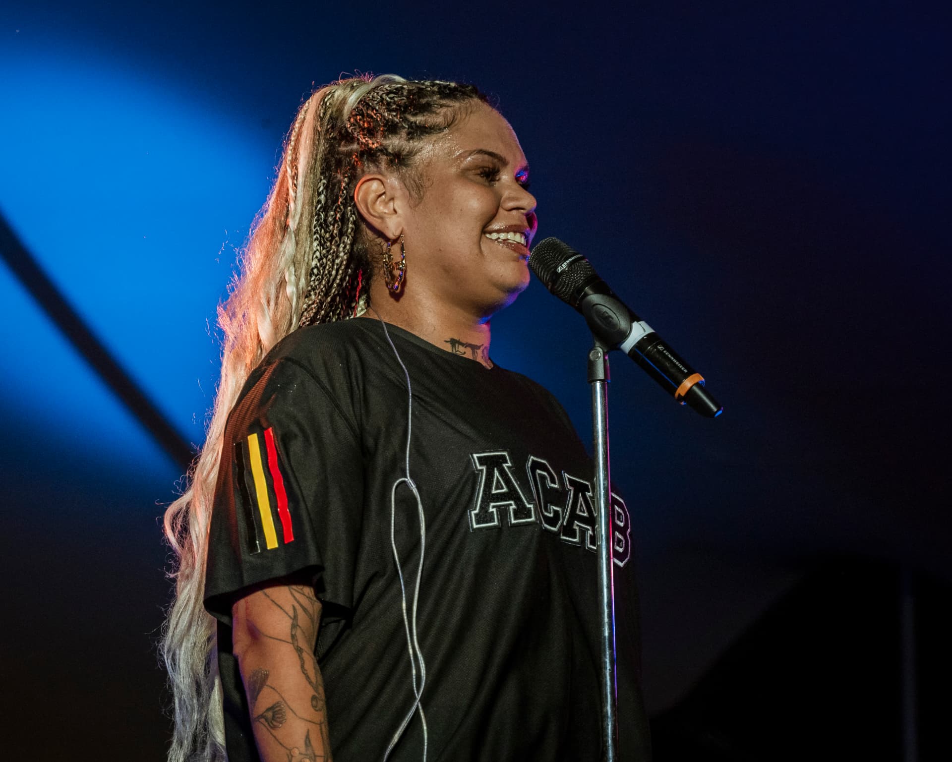 Rapper addressing the crowd in a black jersey under a blue spotlight
