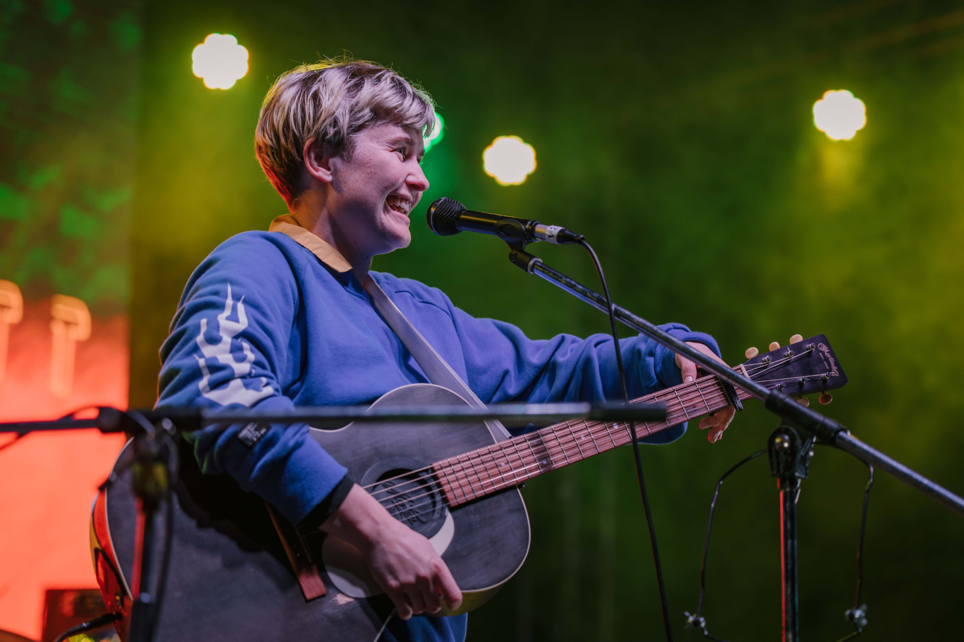 Musician playing an acoustic guitar in a green-lit wash